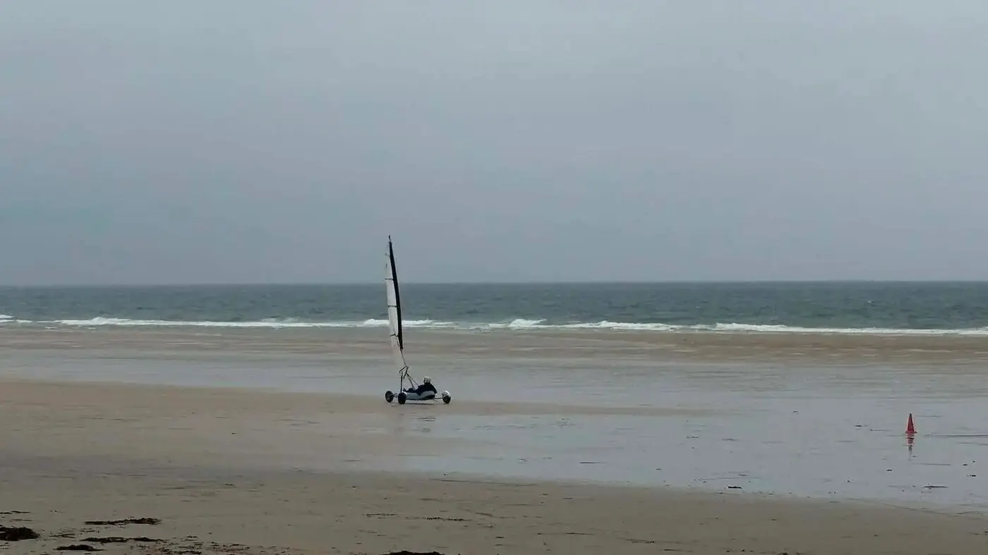Carro a vela che sfreccia su un'ampia spiaggia sabbiosa con la bassa marea lungo la costa normanna, un'avventurosa attività all'aperto per adolescenti